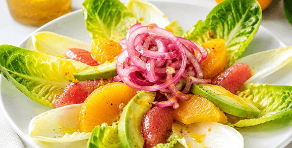 Avocado citrus salad with marinated onion on white plate