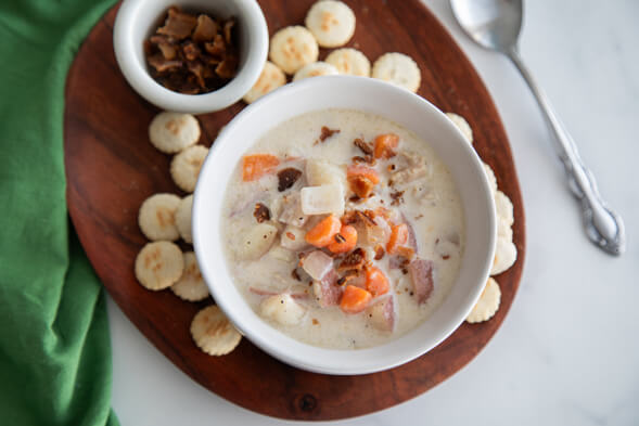 Bowl of New EnglandClamChowder on rown board with soda crackers