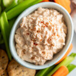 Creamy Onion Dip in white bowl surrounded by vegetables and crackers