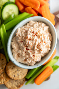 Creamy Onion Dip in white bowl surrounded by vegetables and crackers