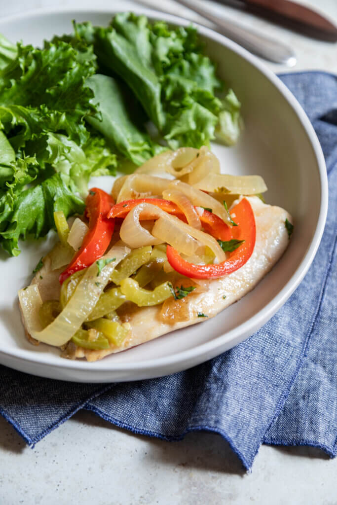 Garden Style Fish with Onions and Peppers on white plate on blue napkin