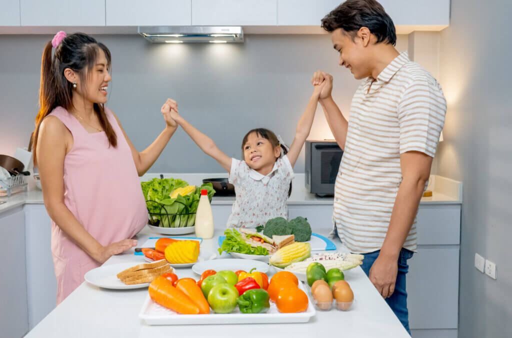 Little  girl hold hands together with father and pregnant mother and stay in kitchen to prepare for cooking with happiness.