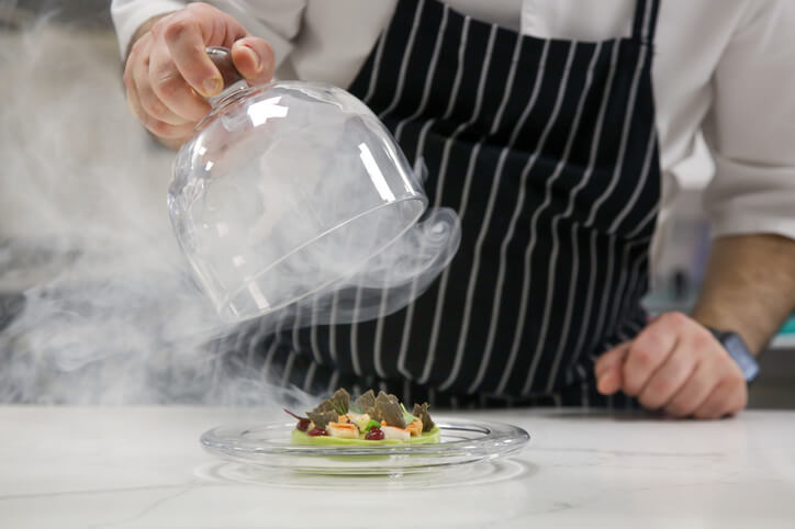 chef pulling glass off plate with smoke billowing out